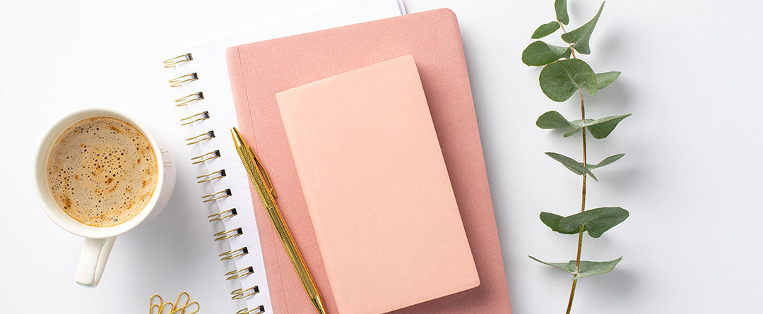 Business concept. Top view photo of workplace stack of pink diar Pink and White dairy standing next to a cup of coffee and a leaf.