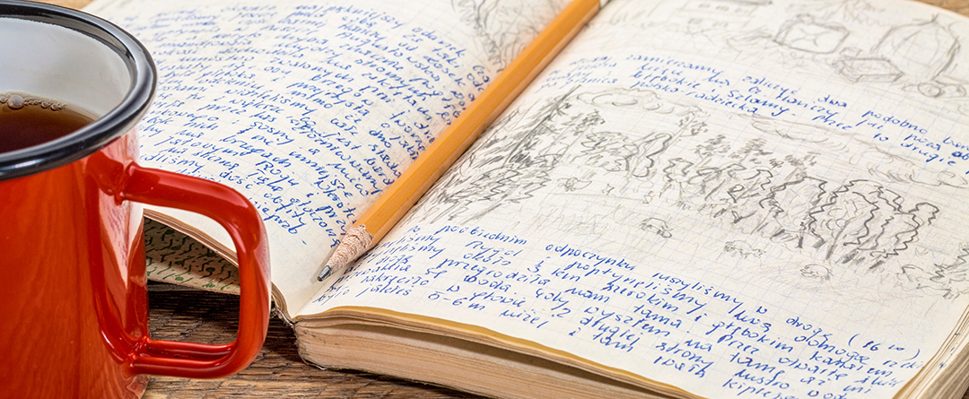 travel expedition journal Journal with lots of writing and erasing with a pencil sitting on top of it next to a red cup of tea.