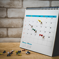 red push pin marked on 29th of white calendar on wooden desk wi